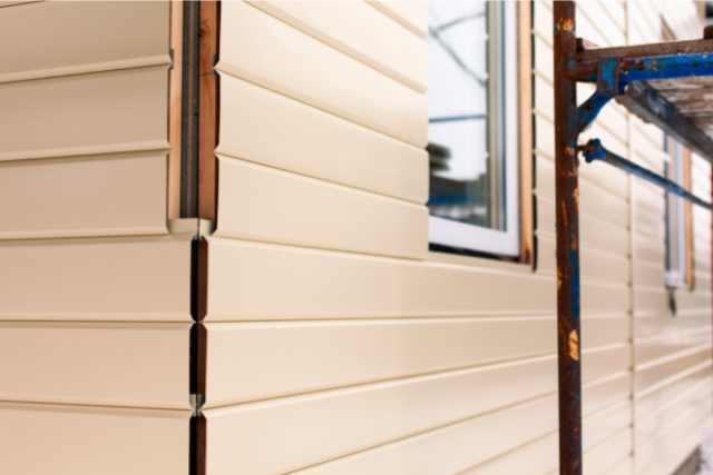 House corner with beige siding covering the walls and scaffolding